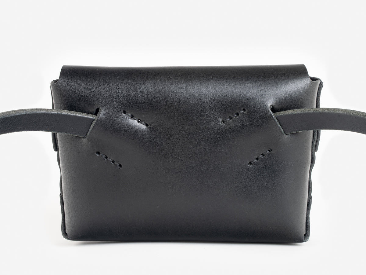Back view of a black leather belt crossbody bag with a smooth finish, featuring  hand-stitching details, displayed against a white background.