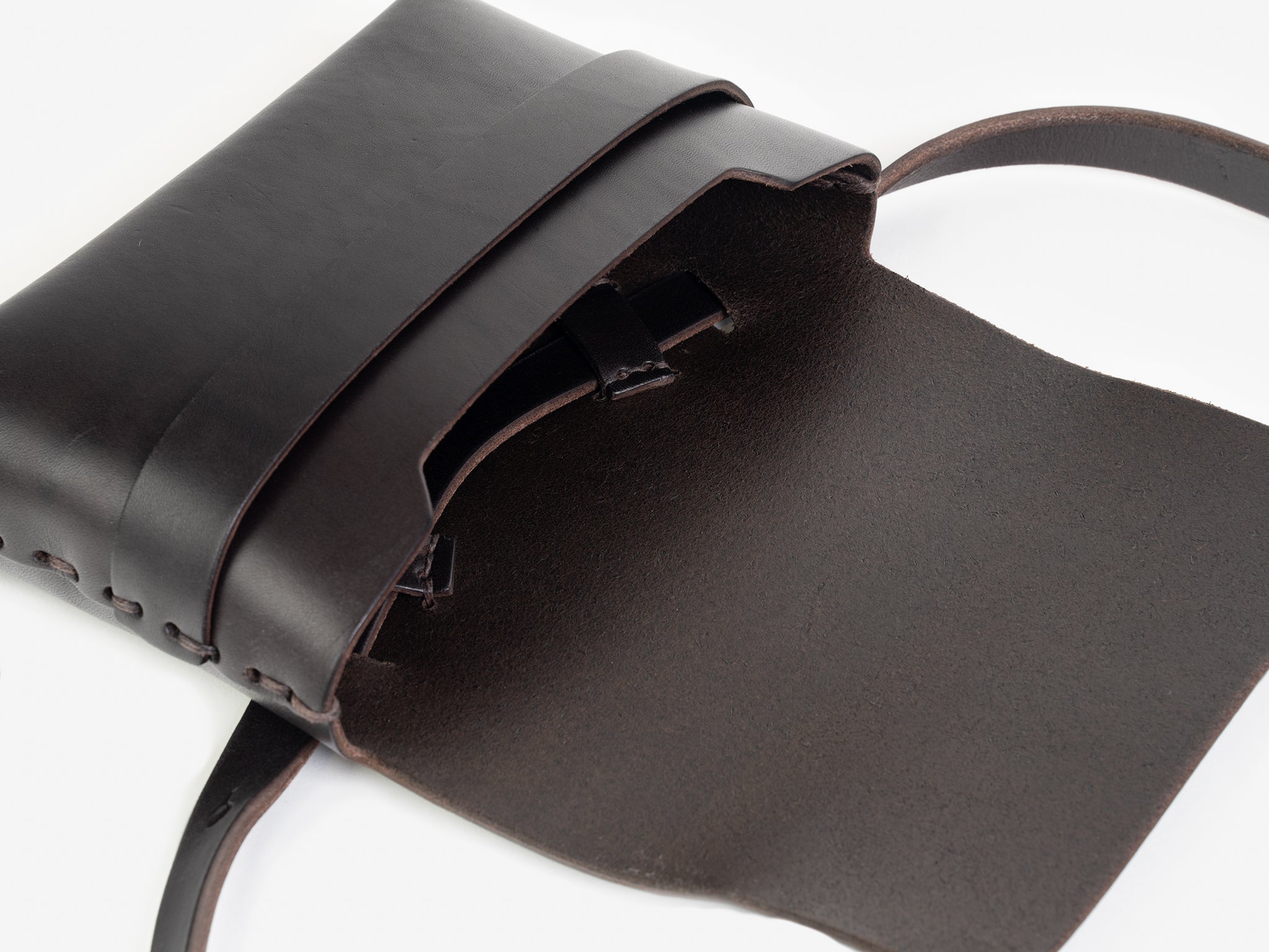 A dark brown leather crossbody bag with a flap open, revealing some hand-stitched details. The bag has a strap and minimalist design, displayed on a white background.