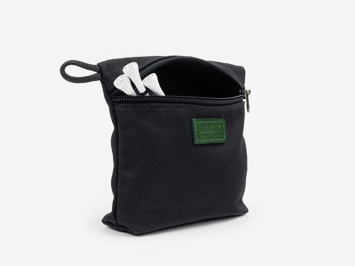 A small black zippered pouch with a green patch, partially open to reveal two white objects inside, against a plain white background.