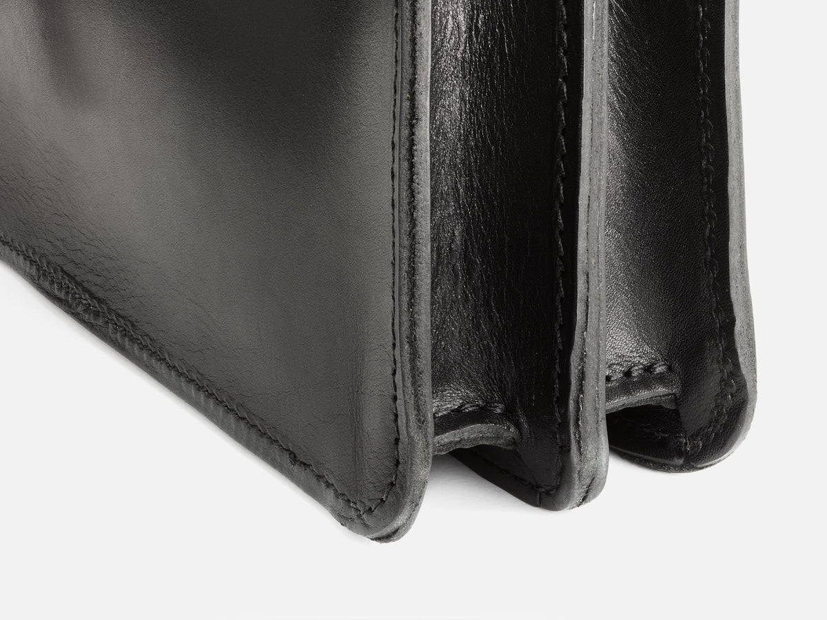 Close-up of the corner and interior sections of a black leather wallet, showing detailed stitching and smooth texture.
