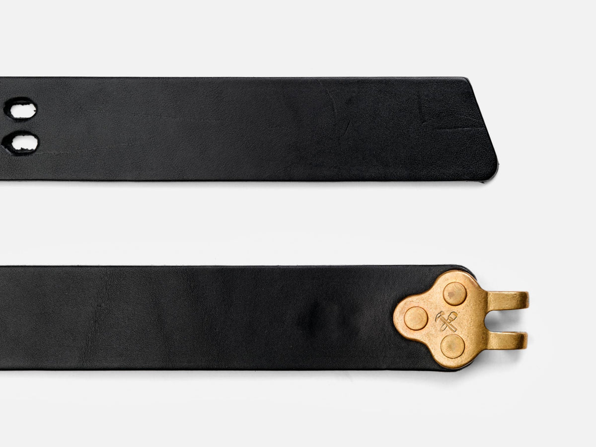 Two black leather belt straps are shown; one has a pointed end and two holes, the other has a gold metal clasp shaped like a bike chain link attached to the end.