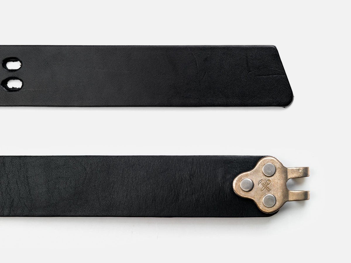 Two black leather belt ends on a white background; one end has two holes, while the other end features a unique metallic clasp with three rivets and a pronged hook.