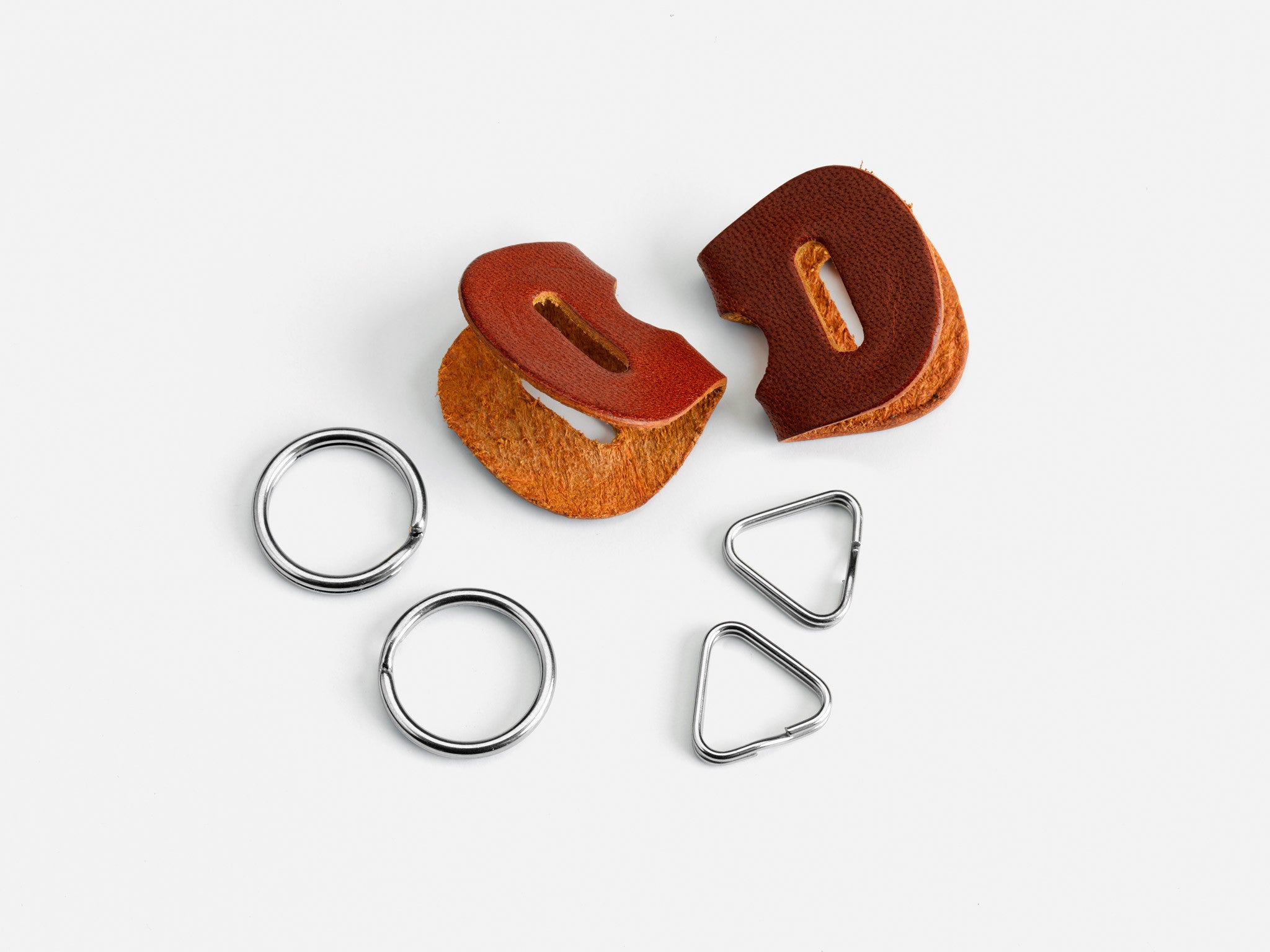 Two brown leather key fob pieces, two silver metal key rings, and two silver metal triangular rings are arranged on a white background.