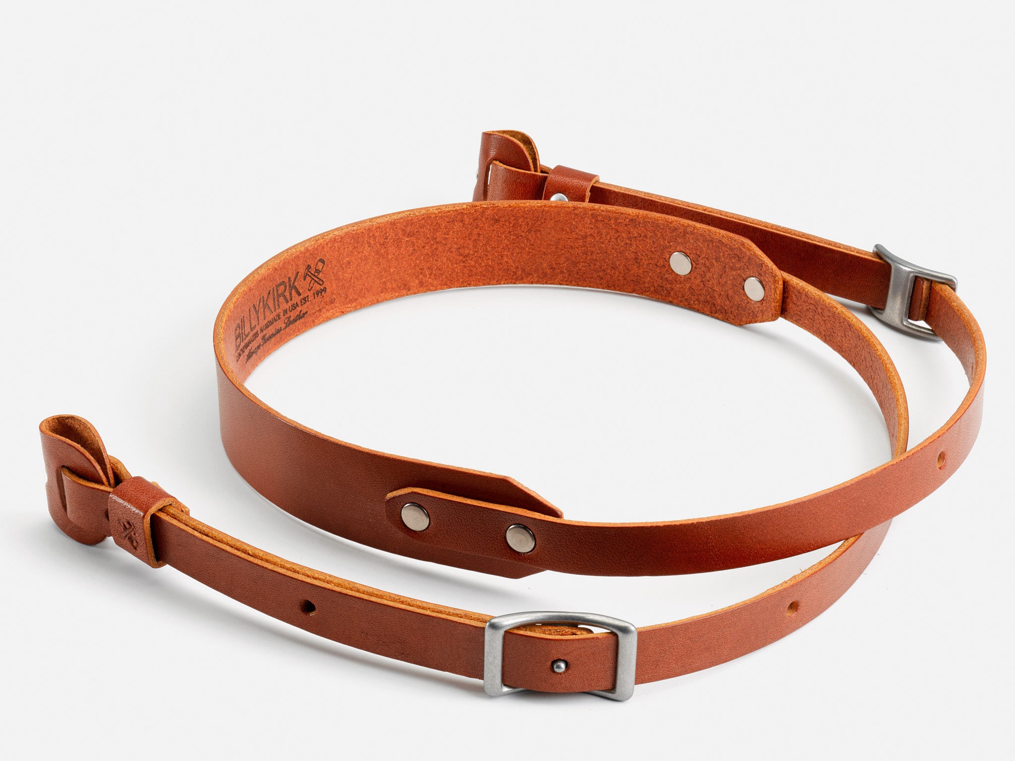 Two brown leather straps with metal buckles and rivets, arranged in a circle on a white background. The inside of one strap displays stamped branding and size information.