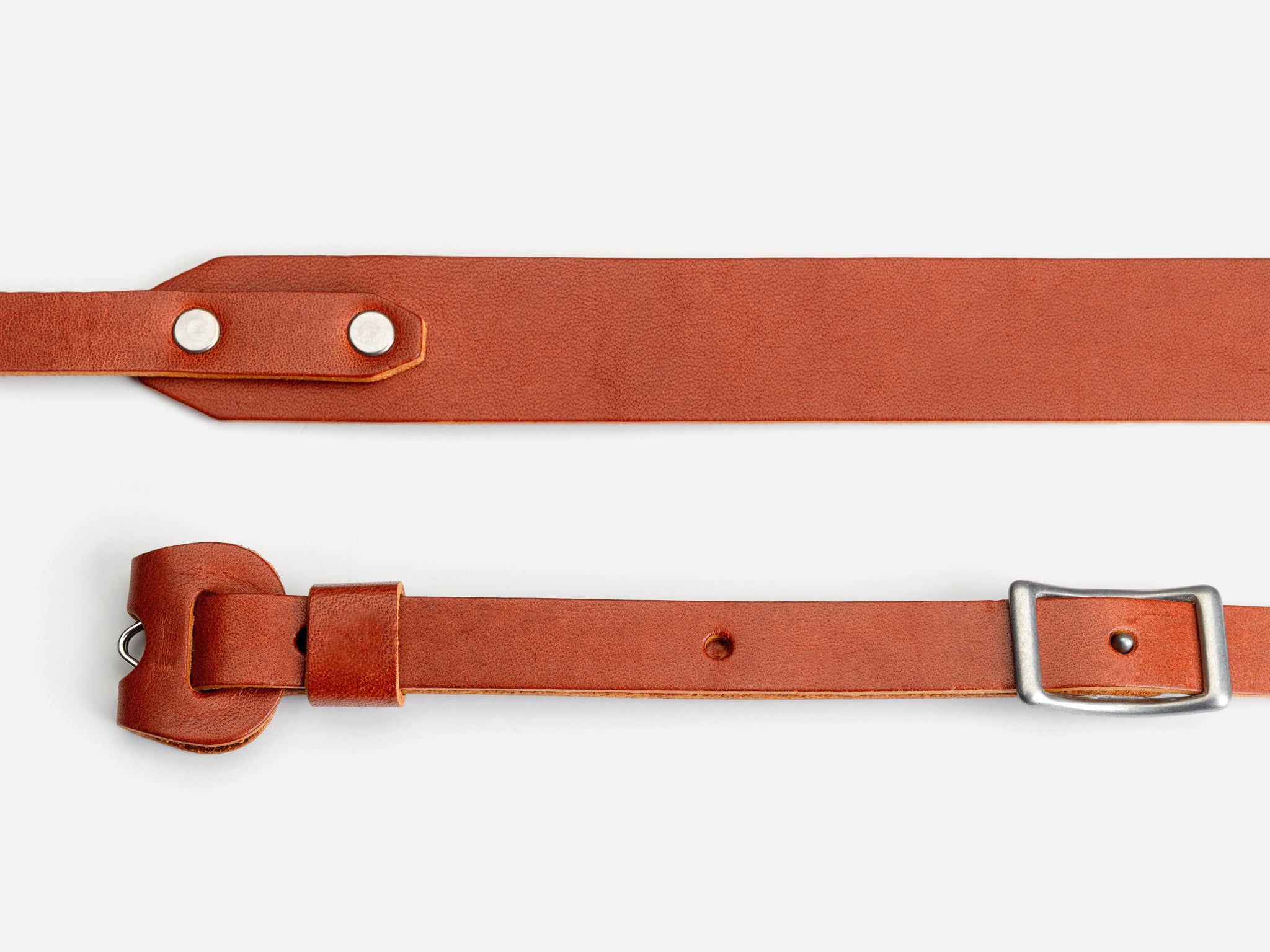 Two brown leather straps laid out on a white background, one with metal rivets and the other with a silver buckle and a rounded end.